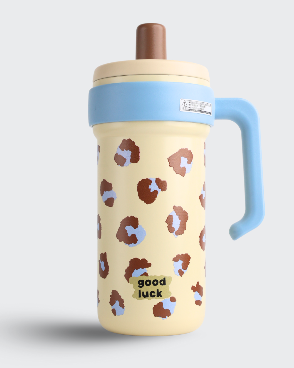 Yellow tumbler with brown pattern and blue handle on a light gray background