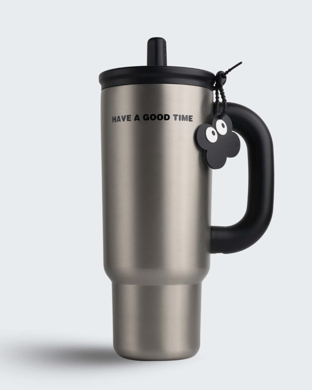Stainless steel travel mug with black handle and tag on a light gray background
